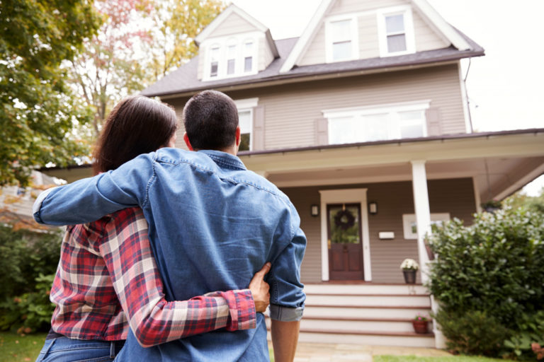 couple embracing each other while looking at a brown house
