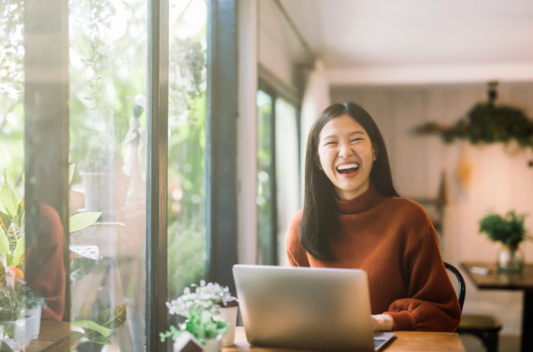 an asian woman smiling while in front of the laptop
