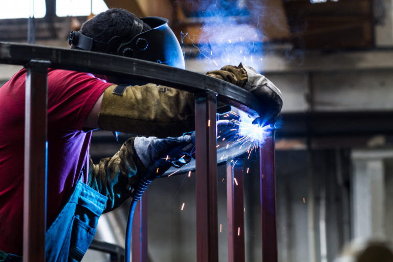 worker wearing ppe welding and fabricating metalworks inside a manufacturing plant