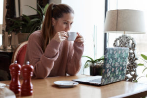 A female freelancer sips a cup of tea while reading emails on her laptop