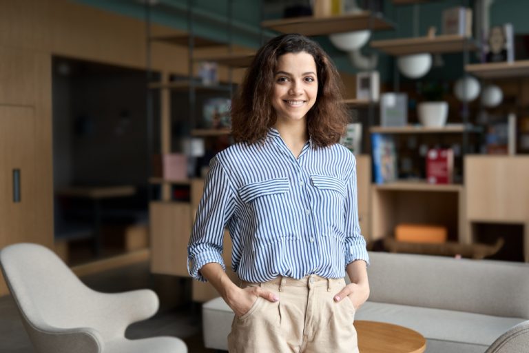 A small business owner smiles with her hands in her pockets while in her home office