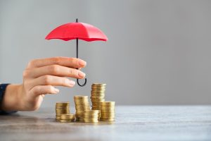 A hand holding a tiny umbrella over stacks of coins