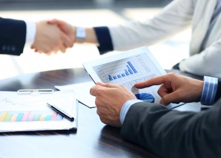 a male businessman holding a digital tablet to view charts with other professionals in the background