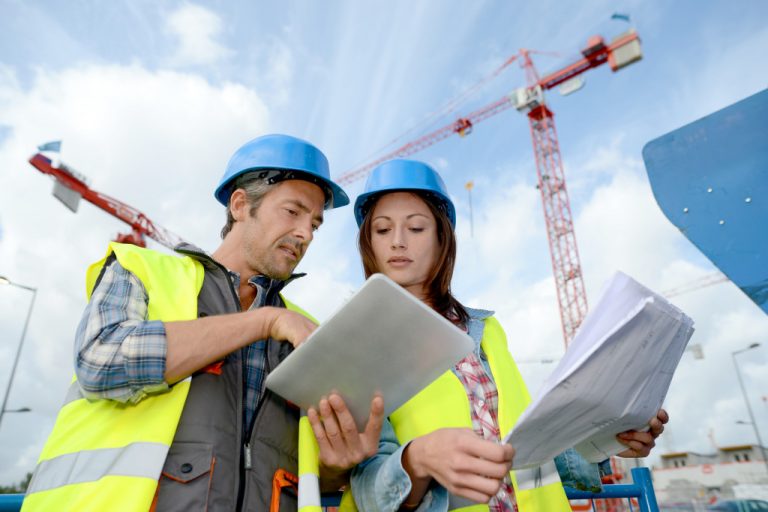 Two engineers looking at blueprint and a tablet on a construction site