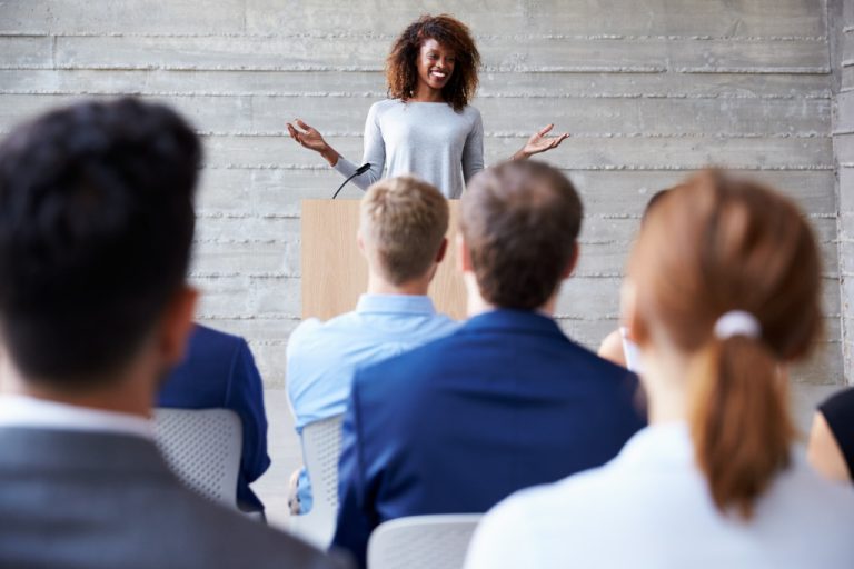 businesswoman smiling while speaking at the podium of a conference