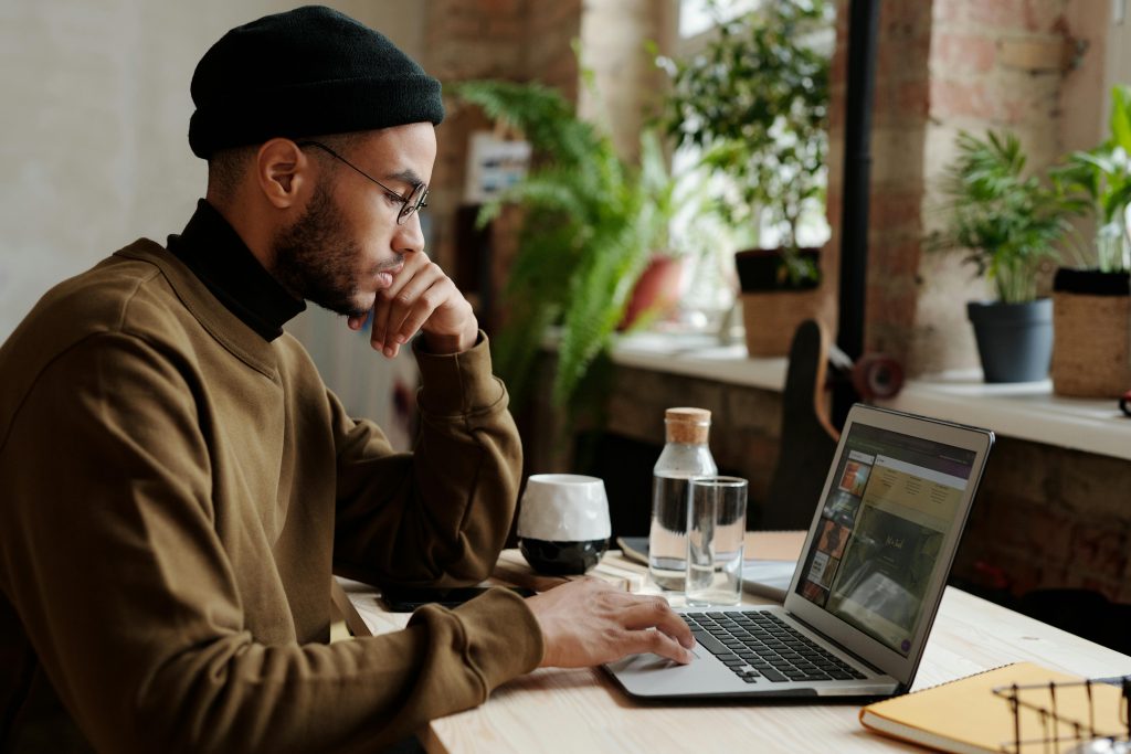 man in a bonnet and eyeglasses intensely focused on the screen of his laptop